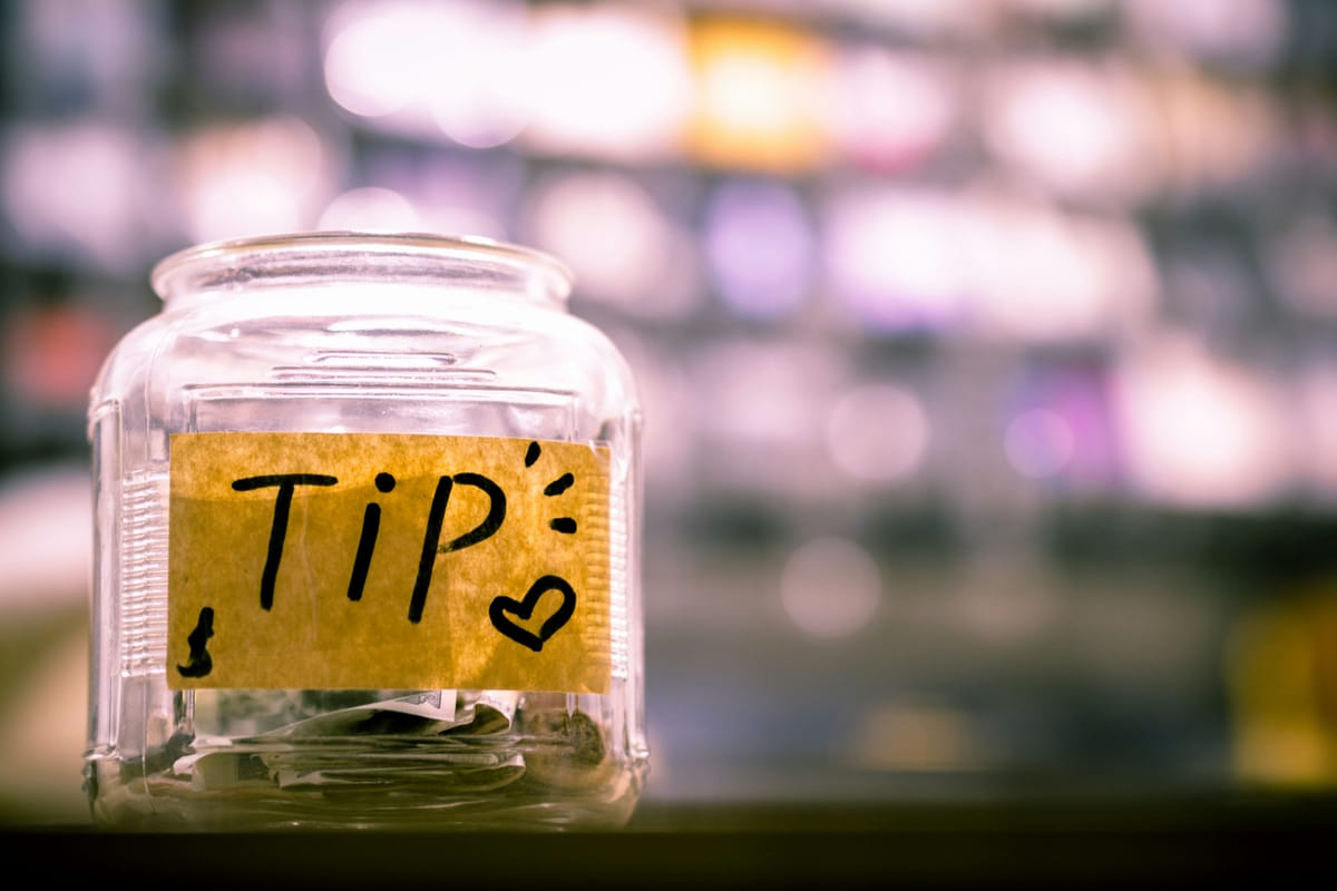 A wide glass jar with a yellow label on it and the word Tip written in black marker.